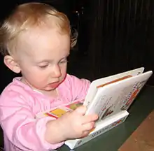 A baby leans at a table staring at a picture book with intense concentration.