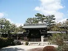 Structure with pointy roof behind a wooden fence and gate.