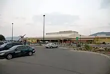 A local parking lot with a number of automobiles using the service; there is also a building of an airport, which contains its terminal.