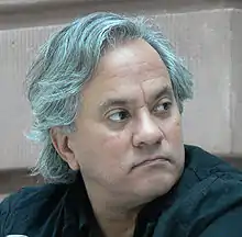 Headshot of an Indian man with gray hair and black shirt