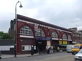 A red-bricked building with a rectangular, white sign reading "KENTISH TOWN STATION" in black letters all under a light blue sky