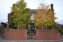 Photograph of a two-story brick house surrounded by a brick wall with rounded corners.