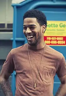 A black male in a red shirt laughs at an off-screen entity