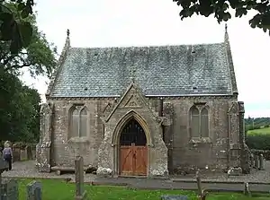 Photo of the castle with the front door closed. The roof is grey in colour, and the building (one storey from this angle) is brown in colour. There are large glass windows which are closed. There are trees on both sides.