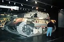 A side view of a large turreted tank in a museum, with sections of its superstructure and turret cut away.