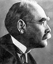 Profile of the balding head of a man in a high collar, tie and coat and with a serious expression. He has bushy eyebrows and a moustache.