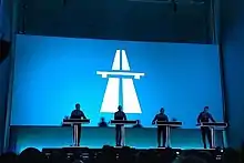 Four figured in shadow on a stage behind a screen projecting the autobahn album cover from the reissue behind them.