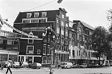 Black and white photograph of assorted buildings in the Wyers complex with a banner which reads "Wyers Inn Holiday Uit", a play on words saying "Wyers In, Holiday Inn out!"