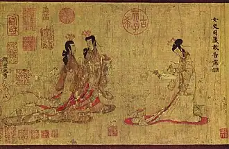 Two ladies walking towards another lady standing at a writing table with a writing brush in her hand