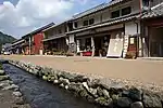 Two-storeyed houses whose ground floor is occupied by shops next to small street and stream.