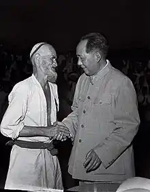 An old bearded Uyghur man shakes hands with a middle-aged Chinese man