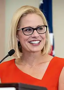 Sinema smiling at a lectern