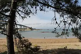 A photograph of a narrow strip of water separating two land masses linked by the Noirmoutier Bridge