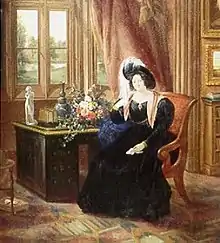 A color picture of an 1833 painting of Lady Tyrconnell sitting in a brown covered chair wearing an 1830s dark blue full dress gown with puffy sleeves, reddish scarf and a dark feathered round hat. She is sitting in the carpeted Gothic-style Drawing room next to a brown desk and light red draped window.