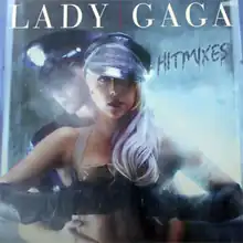 Gaga wearing a hat and gloves, with her hands holding her breasts, and a police officer behind her holding her waist.