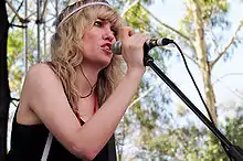 A woman wearing a black singlet and pink hairband, singing into a microphone