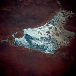 Satellite photograph of an irregularly-shaped body of water, containing numerous small islands, and surrounded by red land marked by numerous parallel lines.