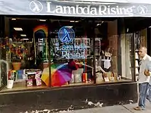 Storefront with an awning reading "Lambda Rising" with "Lambda Rising" neon sign in the window, surrounded by LGBT-themed products.