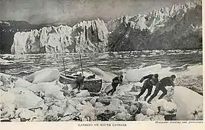 Six men pulling a boat onto an icy shore, with a line of ice cliffs in the background