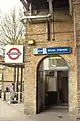 A beige-bricked building with a dark-blue, rectangular sign reading "LATIMER ROAD STATION" in white letters all under a white sky