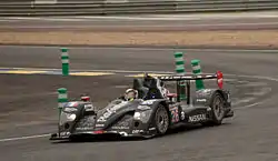 An black open cockpit LMP2 sports prototype car being driven around on a motor racing track