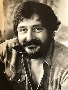 Sepia-toned close-in photograph of a young, bearded man with dark hair, smiling directly at camera