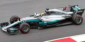 a grey and turquoise open wheeled racing car is driven around a track