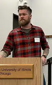 Image 100American man wearing a slim-fitting flannel shirt, a beard, and an undercut, 2019. Sleeve tattoos can be seen. (from 2010s in fashion)