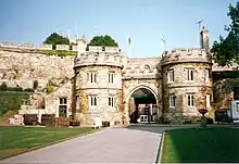 A paved road leading to an arched opening in a tall thick stone wall.