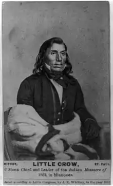 A photograph of a Native American man seated, wearing a suit