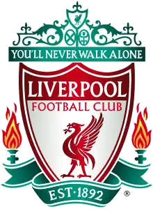 The words "Liverpool Football Club" are in the centre of a pennant, with flames either side. The words "You'll Never Walk Alone" adorn the top of the emblem in a green design, "EST 1892" is at the bottom