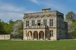 A five-bay, flat-roofed building with two storeys and an arched single-storey portico.  Surrounding the top of the building is a balustrade and chimneys rise from the rear