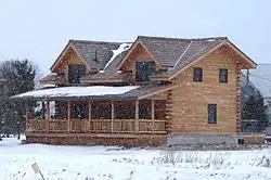 Two-story log house in winter, with large porch and dormer roof