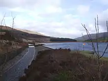 Image 10At the Rhodeswood reservoir dam, we see the outflow canal from the Torside Reservoir dam, alongside the Rhodeswood Reservoir. The Torside dam  can be seen in the distance. To the right is Shining Clough Moss and Bleaklow. To the left Bareholm Moss and Black Hill (from Longdendale Chain)