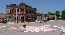 One- and two-story brick buildings seen across a street intersection; crowned eagle painted on the pavement, filling most of the intersection