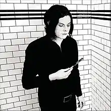 A grayscale picture of Jack White against a wall looking at a shaving razor in his hand