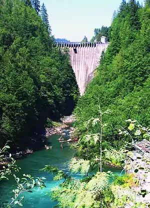 An arch dam straddles a narrow, forested canyon above a tumbling river