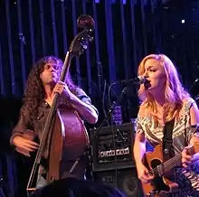 Lydia Loveless singing into a microphone and playing guitar while Ben Lamb plays a stand-up bass