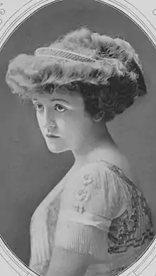 A young white woman with voluminous wavy hair in an updo, wearing a dress with short fringed sleeves.