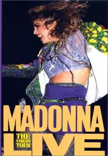 Madonna dancing while looking towards her right. She is clad in a brightly colored jacket and a purple skirt, with a crucifix hanging from her neck.