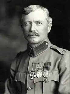 A black-and-white portrait photograph of a blond-haired white man in military uniform. He has a well-groomed moustache, bright eyes, sharply cut hair and a row of medals on his chest.