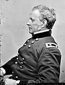 Black and white photo of a clean-shaven man wearing a dark military uniform with the shoulder tabs of a major general (two stars). The photo is taken in profile with the subject looking to the viewer's left.