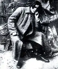 Portrait photograph of Nestor Makhno, seated, wearing a long military jacket and boots