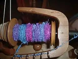 A reel of handspun bouclé yarn in blue, purple and pink. The effect yarn has created a densely-packed series of small loops.