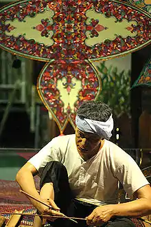 Making a traditional Wau jala budi kite in Malaysia. The bamboo frame is covered with plain paper and then decorated with multiple layers of shaped paper and foil.