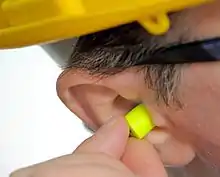 A man inserting an earplug in his ear to reduce his noise exposure