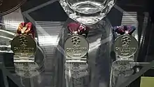 A photograph of three medals sitting on a stand. One medal is gold and two are silver.