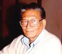 A photograph of an old man wearing blue suit and glasses.