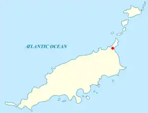 Map of an archipelago in the Atlantic Ocean. The main island is rod-shaped, oriented approximately west-southwest to east-northeast, with some irregular features in the coastline. A red label at the northeastern tip. Off the southern coast are nine smaller islands. Off the northeastern tip of the main island are five other smaller islands.