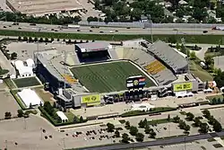 A soccer stadium with a grass field, crowds in the stands, a distant scoreboard, and a blimp flying overhead during the game.